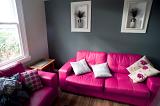 Stylish living room with pink and grey decor with a comfortable bright pink leather lounge suite with floral cushions