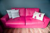Stylish pink leather sofa with elegant cushions on a hardwood floor against a grey wall in an interior decor concept
