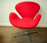 Retro-style chair with a molded modular design in red and a steel base standing on a brown carpet against a white wall in an interior decor concept