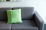 Grey upholstered sofa with a green cushion with button detail, close up view