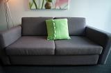 Wide angle close up view of an empty upholstered modern grey couch with a green cushion