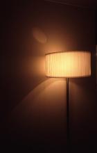 Illuminated standard lamp with an modern styled pleated lampshade shining in the darkness