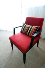 Upholstered maroon armchair with a decorative striped cushion standing in front of a large floor length window