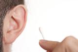 a man holding a cotton bud with his ear out of focus in the background