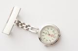 Silver metal nurses fob watch with blank name tag and chain lying diagonally on a white background with copy space