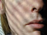 Close up of the sullen glum mouth of a young man with an unshaven upper lip with bristle taken in dappled sunlight with line shadows - concept of mental health