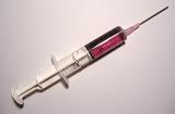 White plastic syringe filled with a dose of pink soluble medicine for an intravenous injection, close-up with copy space on gray