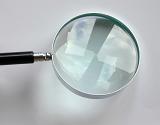 Reflections in the lens of a small round metal magnifying glass for visual enlargement over a light grey background