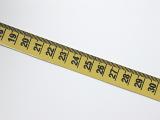 Extended yellow tape measure marked in centimetres for measurement of length and distance lying diagonally on a white background with copyspace