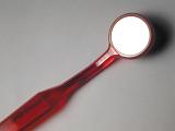 Small red plastic mirror on a long neck for dental examination to check for caries of the teeth or oral problems diagonally on a grey background
