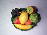 Bowl of fake fresh fruit with colorful wooden imitations viewed from overhead over a grey background
