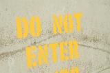 Do Not Enter yellow sign painted through the stencil on grey wall, viewed in close-up and full frame