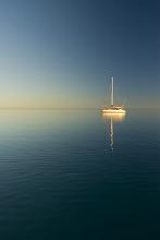 lookout out across still water, a lone yacht moored in a sunset glow