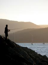 a man fishing at sunset from a marina wall