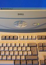 Old DELL personal computer with keyboard and monitor in cropped close-up vertical photo with Windows OS on the blue screen, navigation arrows and power button with green led lamp