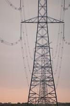 Electric pylon with high voltage cables distributing electricity on the grid viewed at sunset or sunrise against a pale pink orange sky