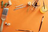 Art and craft concept background decorated with paintbrushes, wire and spools over orange copy space in the middle