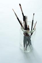 Glass jar with assorted paintbrushes in different sizes and shapes of bristle for art, high angle over a grey background