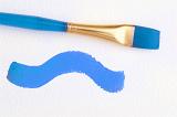 Blue paintbrush with a painted wavy line of blue paint on a textured white paper in a concept of art and creativity