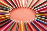 Circle shape formed by various multicolored sharp colored pencils over red background