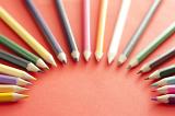 An arch shape of various selected colored pencil tips pointing toward each other over red background