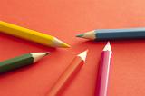 Close up of five colored pencils, yellow, red, pink, blue and green, over orange background