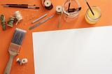 Blank paper surrounded by paint brushes, spools, thread, wire, blades and pins over orange background