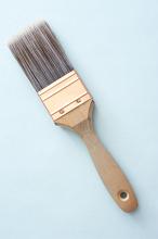 New paintbrush for interior decor with bristles and a wooden handle viewed from above diagonally on a blue background with copyspace