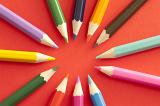Ring of various sharpened colored pencil tips pointing toward each other over bright red background