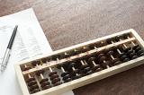 Wooden abacus being used for accounting lying on a desk with a balance sheet and ballpoint pen viewed from above