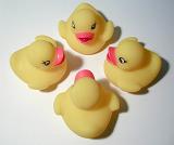 Four cute little toy yellow rubber ducks arranged facing each other in a circle, high angle view on grey