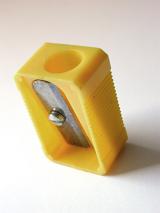 Yellow plastic pencil sharpener standing upright on white with the blade towards the camera