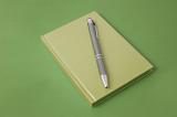 Ball pen and green notebook on green background