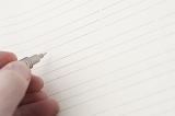 Hand holding a mechanical pencil over a blank page ruled with lines for your message or text