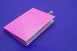 Closed pink notebook with pen inside on purple background