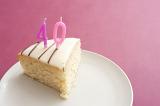 Slice of cake with burning 40th birthday candles served on a plate over a pink background with copysace