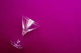 Empty martini cocktail glass lying on its side in the corner on a maroon background with copy space for your festive party greeting or invitation
