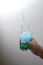 Man holding a blue cocktail party drink with decorative bendy straw in a star shape over a grey background