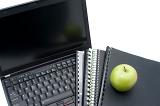 Study concept closeup of an open laptop, with workbooks and notebooks and a fresh green apple