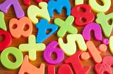 Close up showing fridge magnets of numbers and mathematical symbols, in bright colours over wood effect background