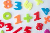 Fridge magnet numbers and mathematical symbols, in bright colours over white background